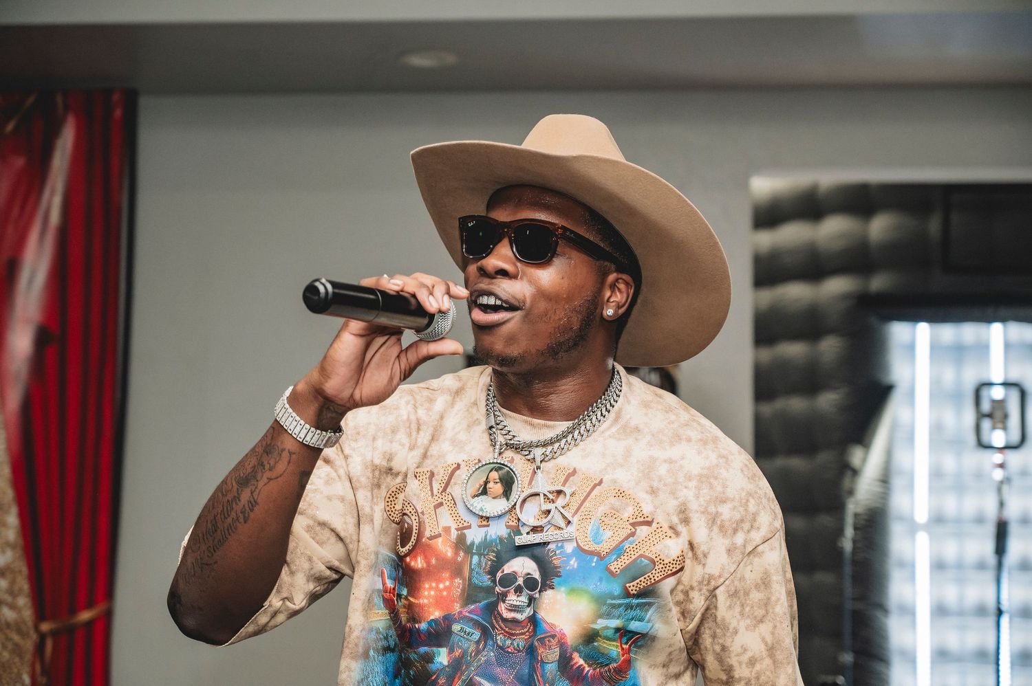 Singer wearing tan cowboy hat and graphic t-shirt performs energetically with microphone on stage.