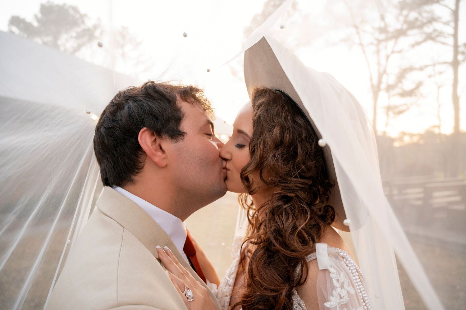 A couple shares a romantic kiss in a dreamy outdoor setting with sunlight streaming through the trees.