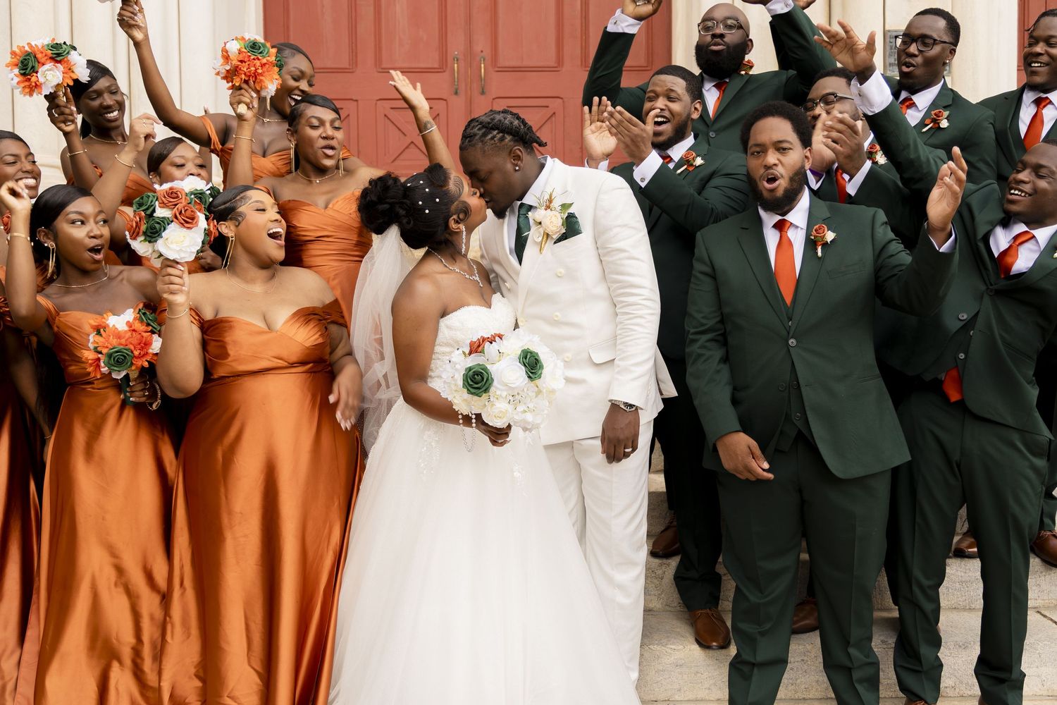 Wedding party members in burnt orange dresses and dark suits celebrate joyfully at an elegant ceremony.