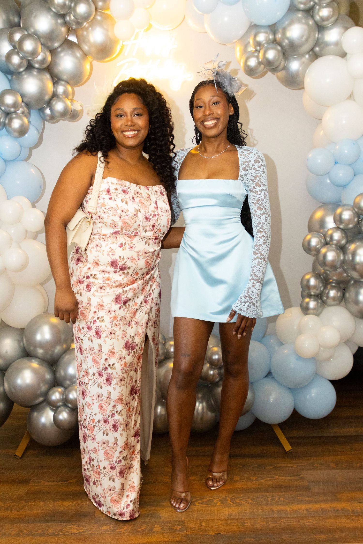 Two people pose together in front of a silver and blue balloon arch backdrop during a celebration event.