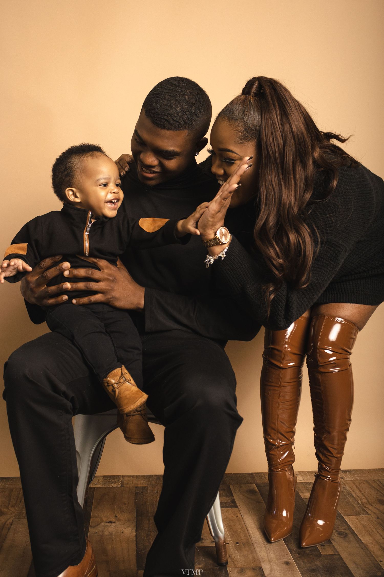 Young Black family in matching black outfits poses for a studio portrait with their smiling baby boy.