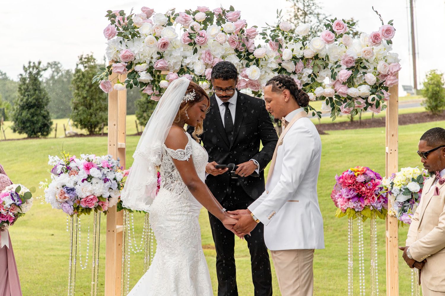Bride and groom exchange rings at floral arch during outdoor wedding ceremony on golf course.