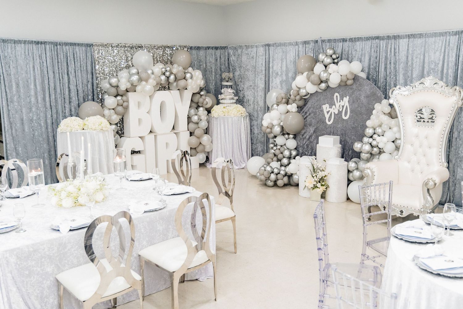 Elegant wedding reception setup with white and silver decor featuring multiple round tables in a spacious banquet hall.