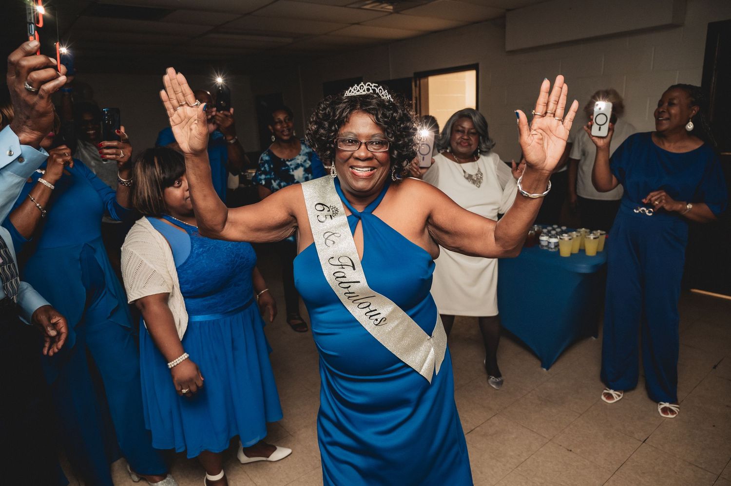 Group of party guests in blue dresses dancing and celebrating at an indoor event.