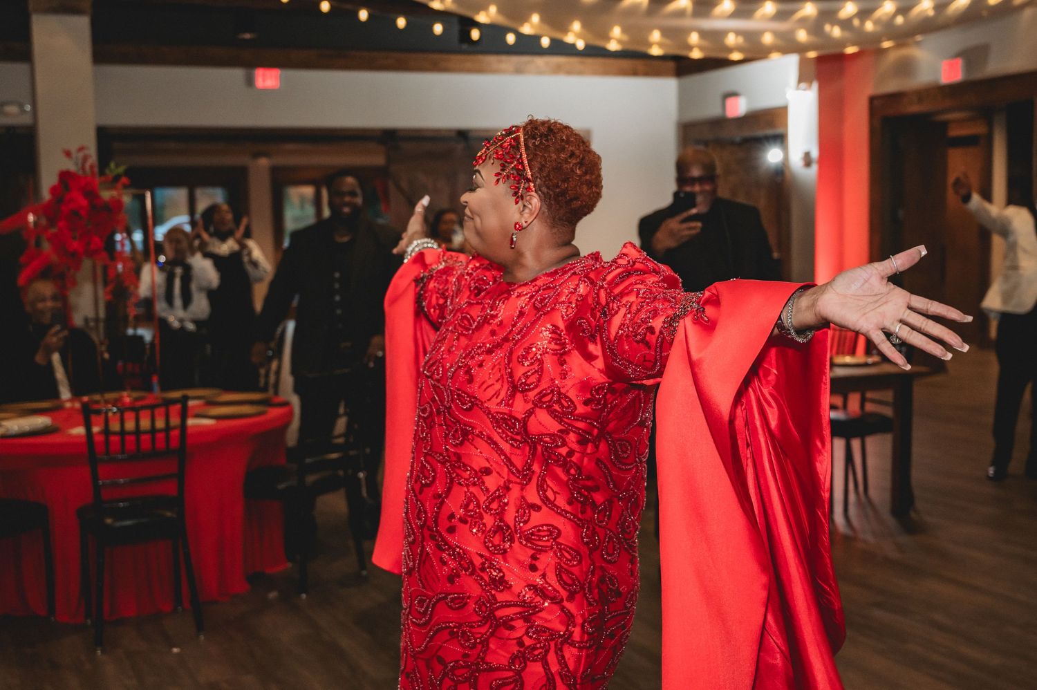 Party guests dancing and mingling beneath string lights at an elegant indoor event with red decor accents.