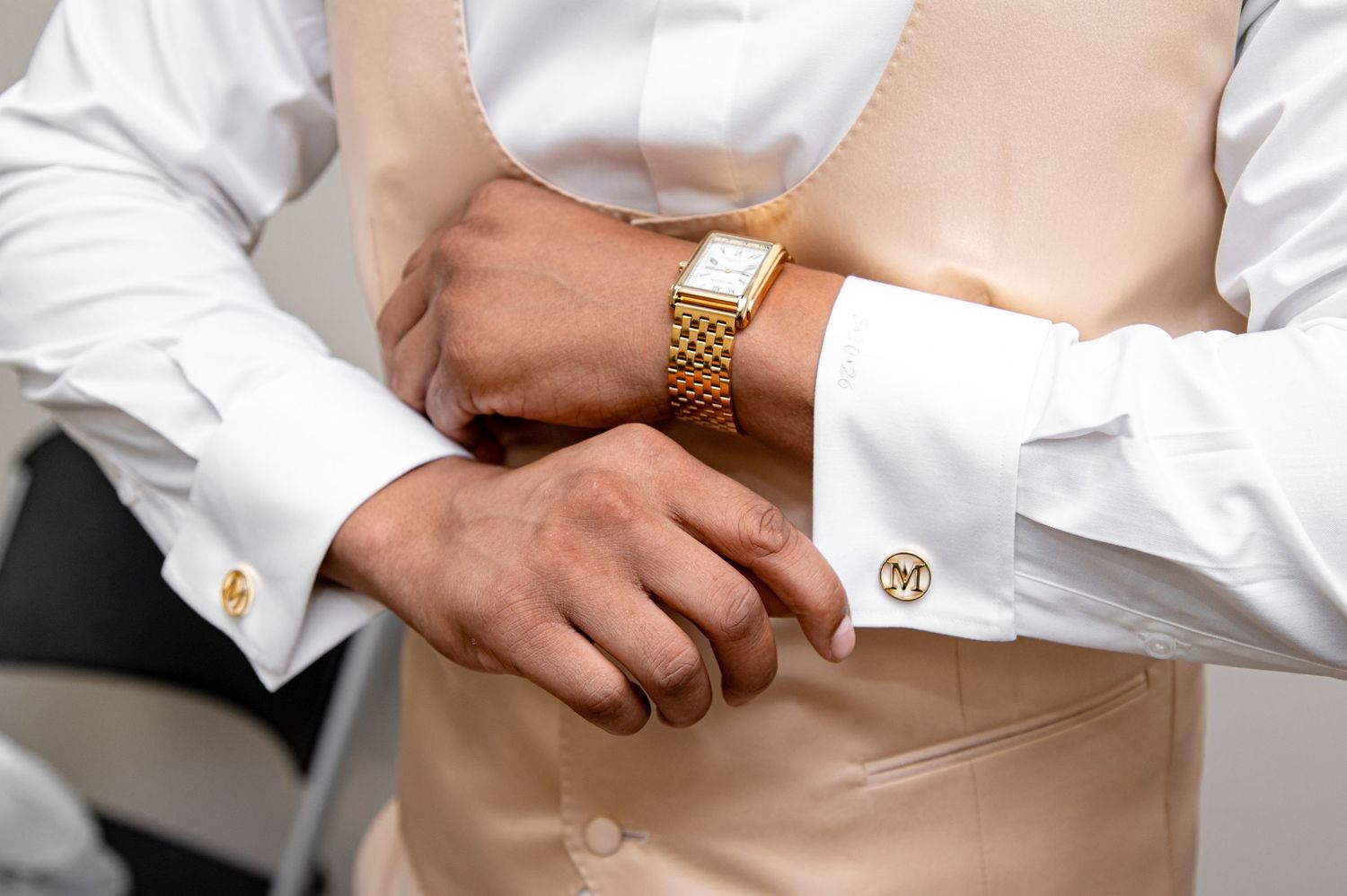 Close-up of groom adjusting cufflinks wearing a gold watch, white shirt, and monogrammed cufflinks.