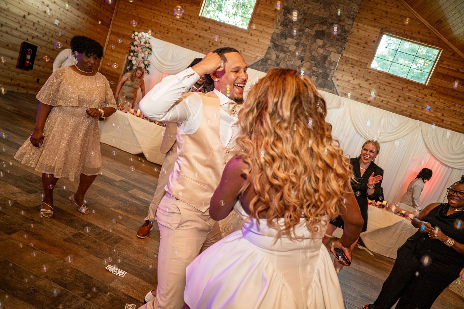 Newlyweds sharing first dance surrounded by bubbles at rustic wedding reception.