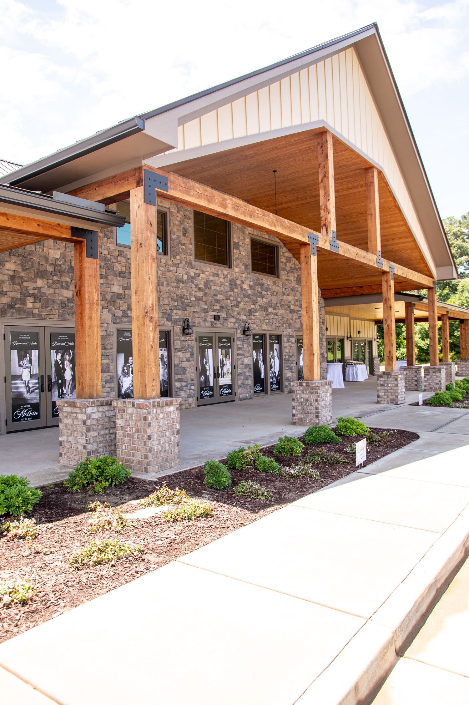 Modern wedding venue exterior with brick columns, wood beams, and black-and-white door displays under a covered entrance.