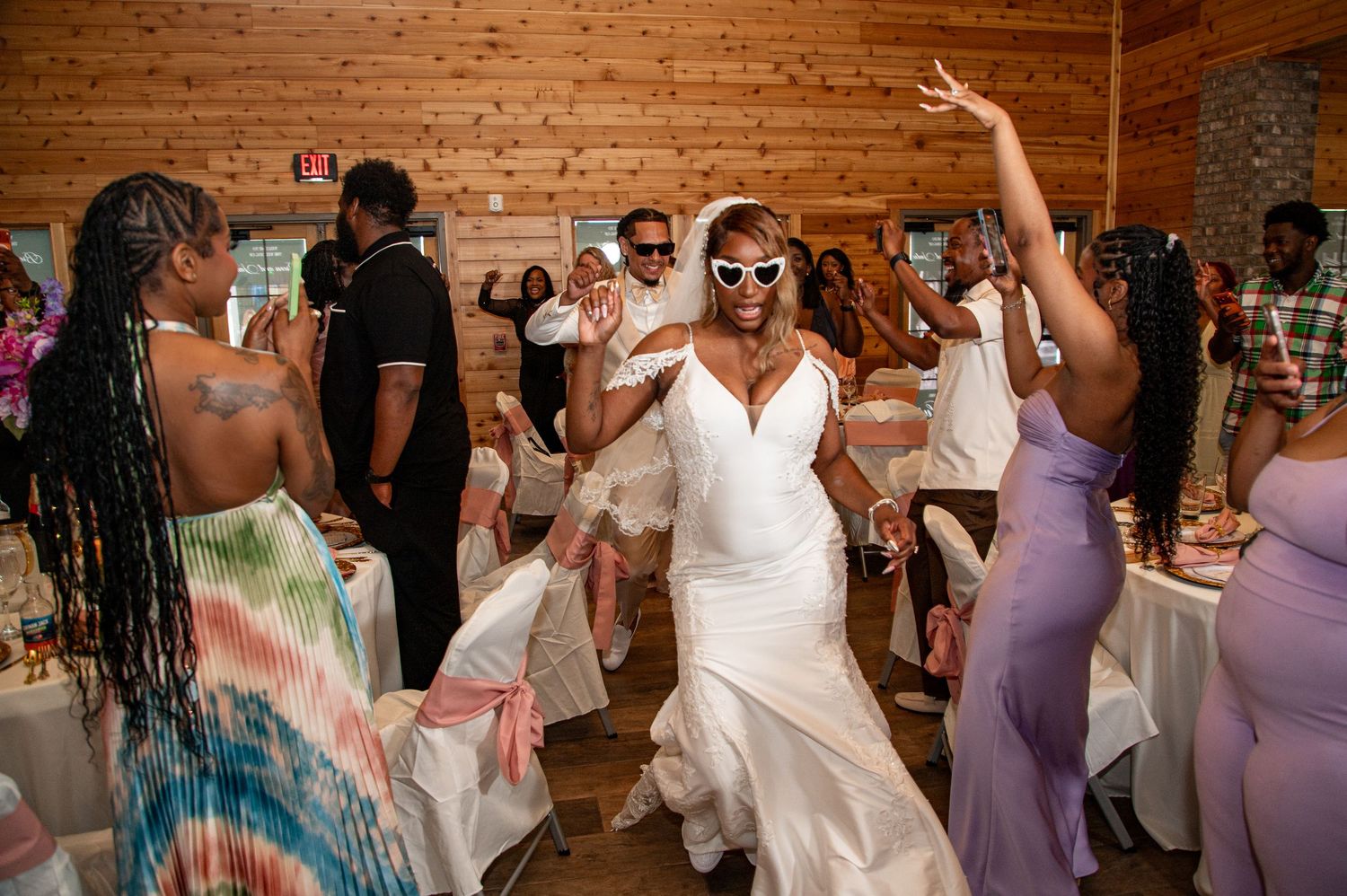 Bride in white gown dancing joyfully with sunglasses at wedding reception.