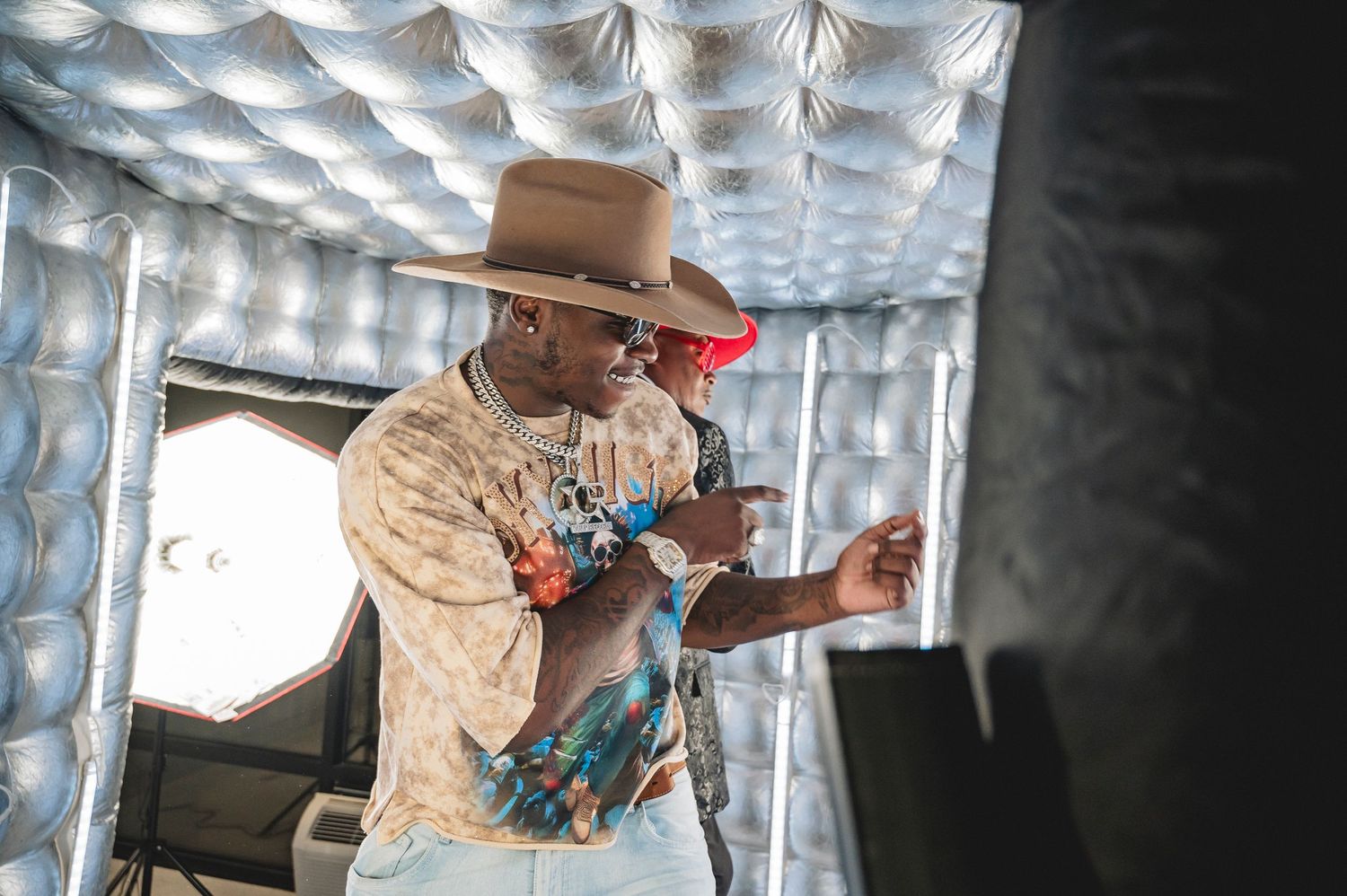 Performer in cowboy hat and patterned shirt performs under dramatic ceiling lighting.