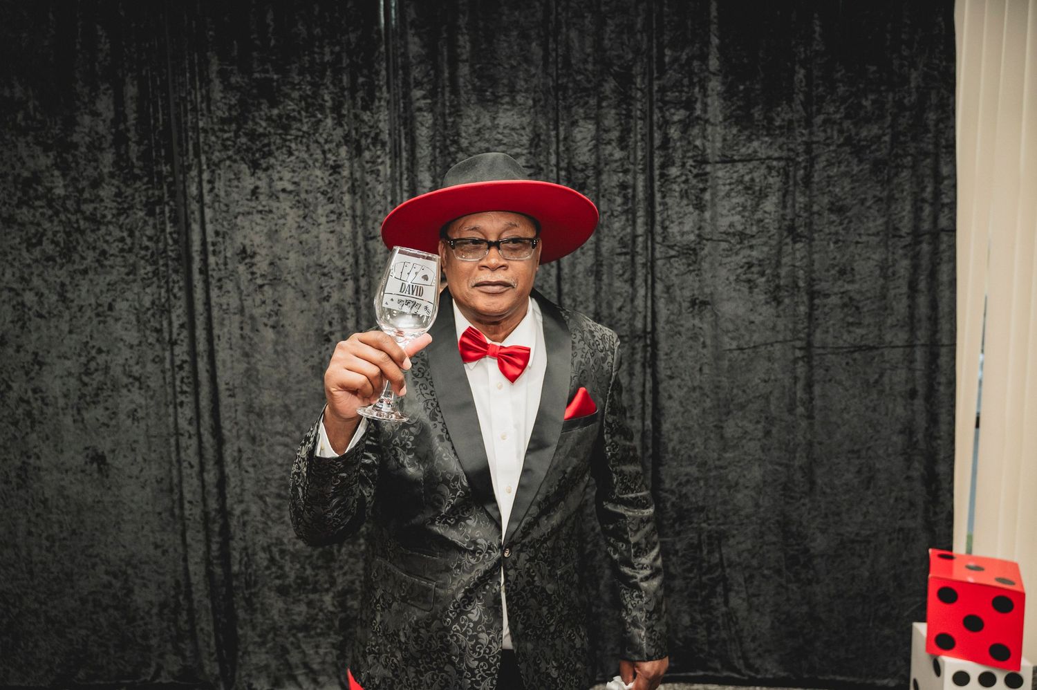 A person in formal attire with a red hat raises a glass at a casino-themed party.