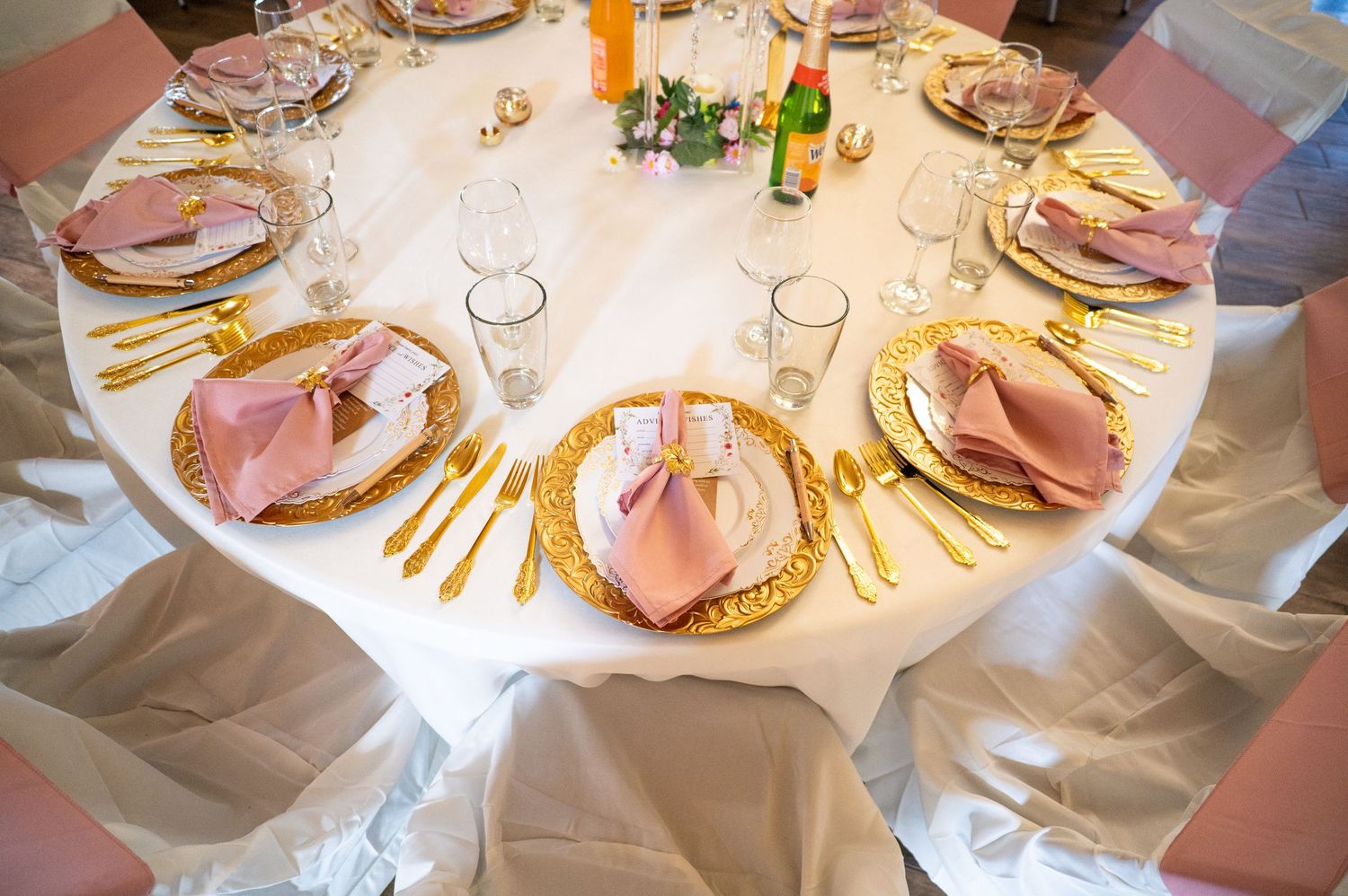 Elegant wedding reception table set with gold chargers, pink napkins, gold flatware, and crystal glassware.