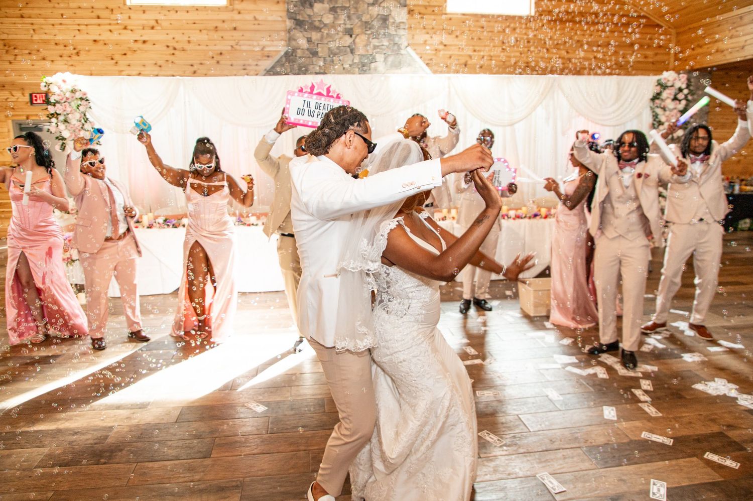 Bride and groom share first dance surrounded by wedding party in rustic barn reception venue.