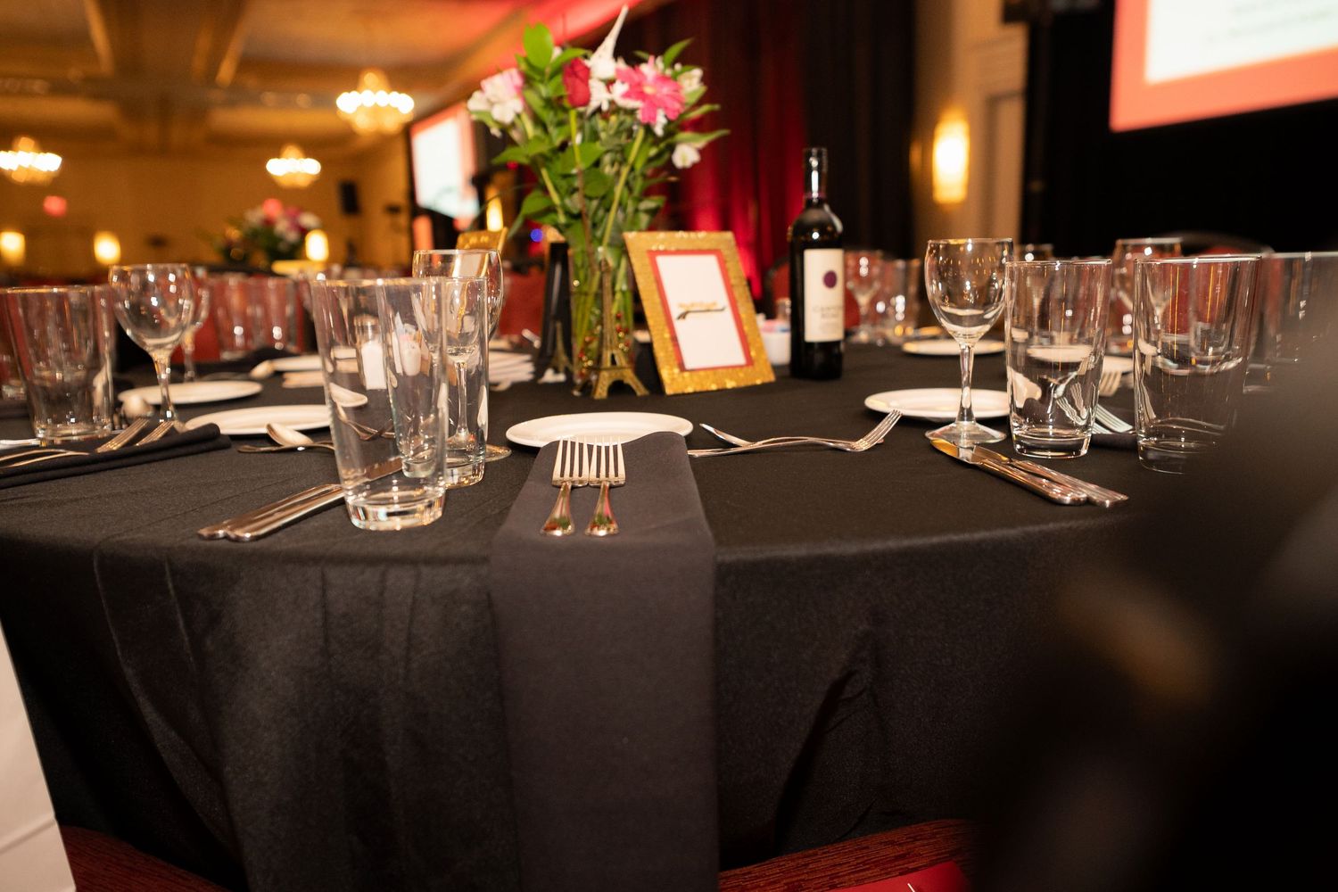Elegant restaurant interior with dark tables set with white linens and glassware under warm lighting.