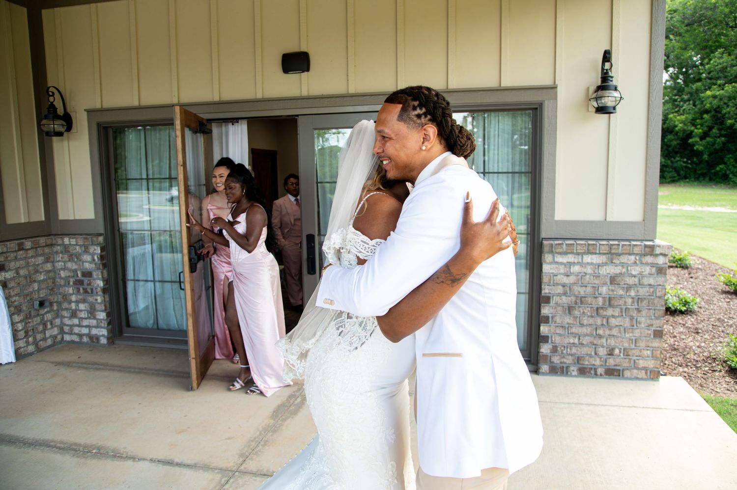 Bride and groom sharing emotional first look hug at wedding venue entrance.