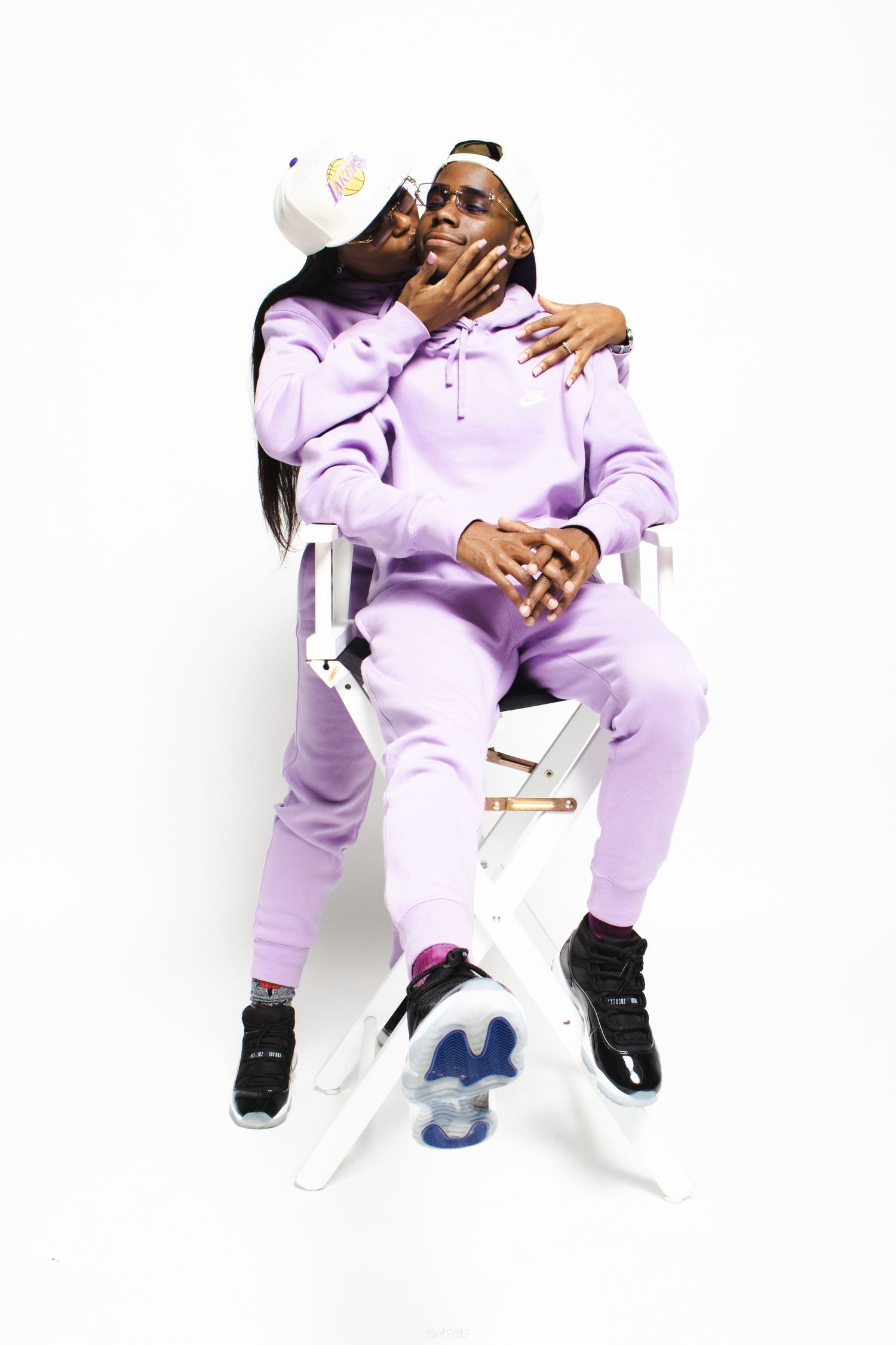 Couple in matching lavender hoodies and joggers posing together on white chair with black sneakers.