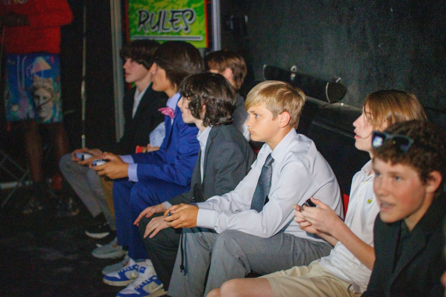 A group of people sitting together at a cluttered table with hands on game controllers during an indoor gaming session.