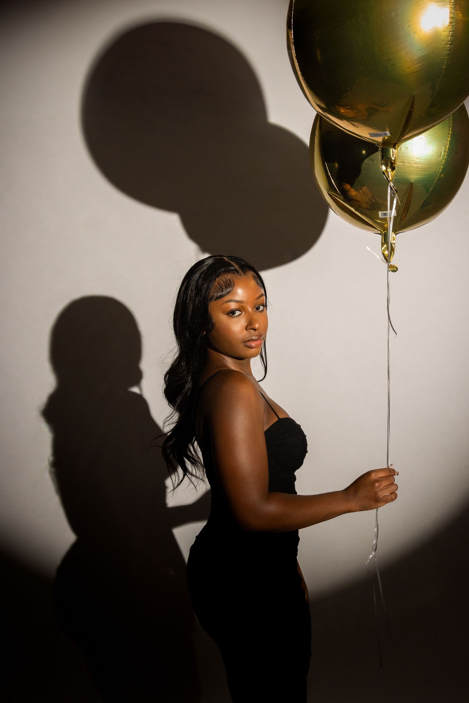 A dramatic portrait series with gold balloons and shadow play against a white wall creating an artistic silhouette effect.