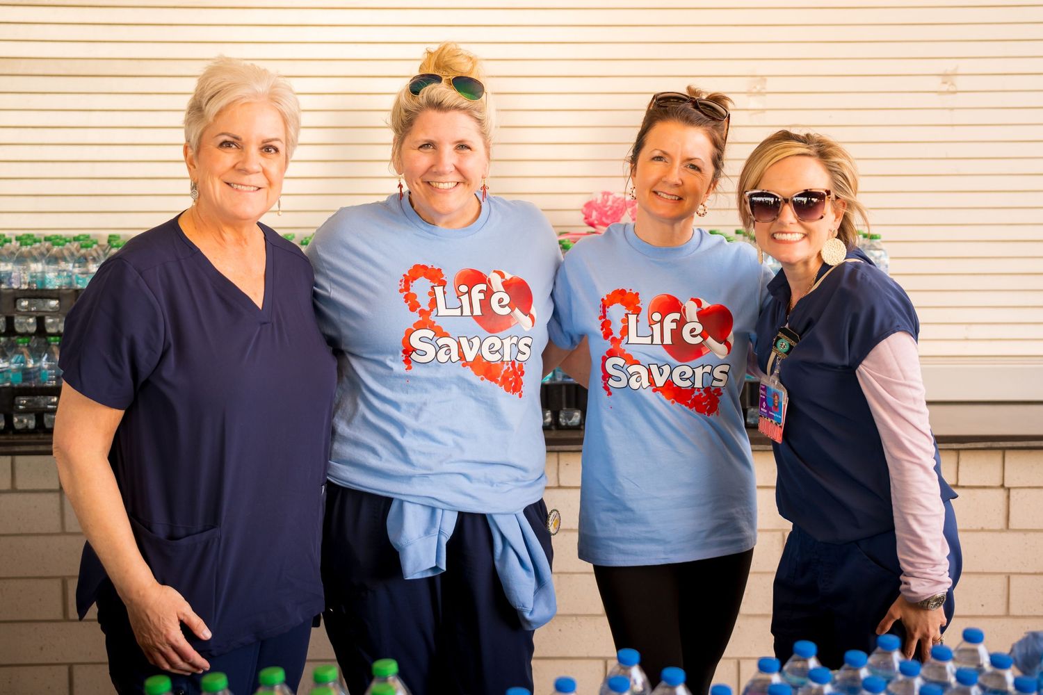 A group of healthcare volunteers wearing matching light blue t-shirts gather together outside a building.