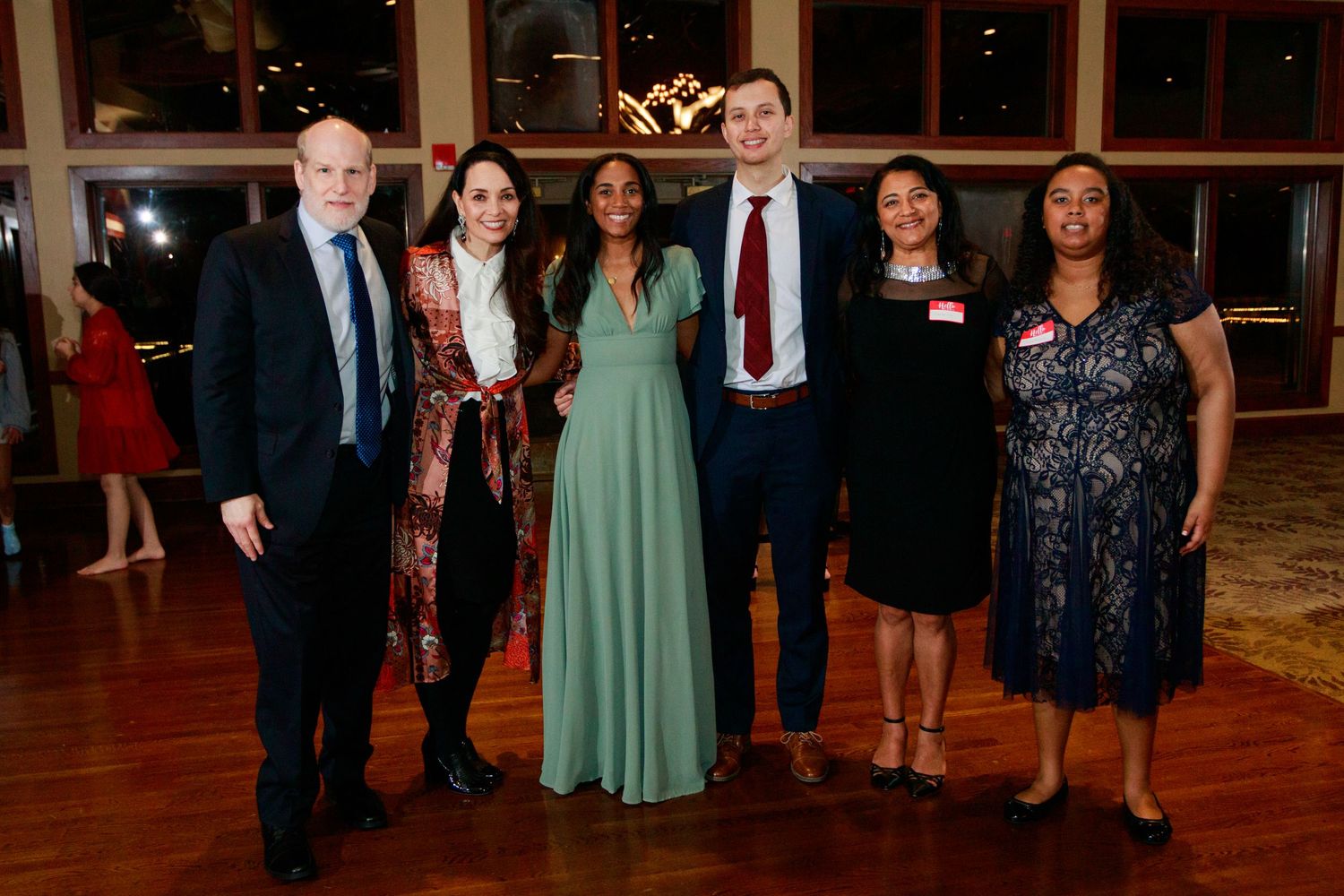 Six professionally dressed individuals posing together at an elegant formal event in a warmly lit venue.