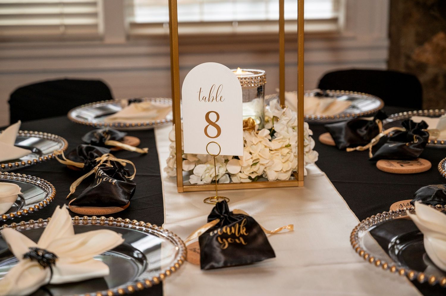 Elegant black and gold wedding reception table settings with place cards and decorative elements in warm lighting.