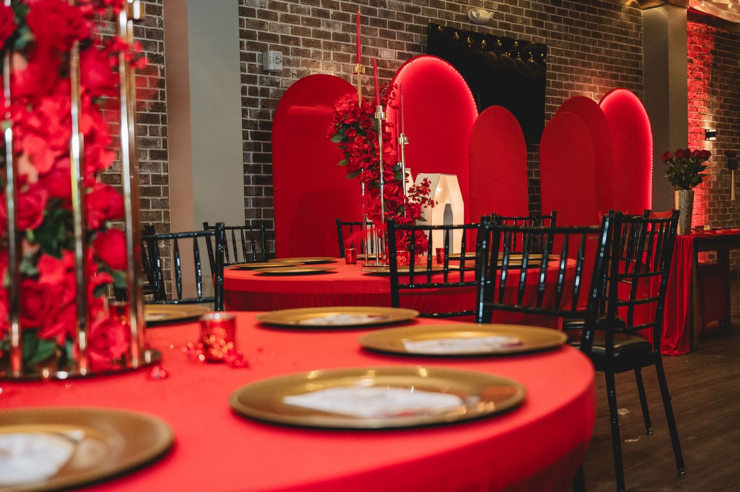 Elegant event venue with brick walls, dramatic red lighting, and romantic table settings for a special occasion.