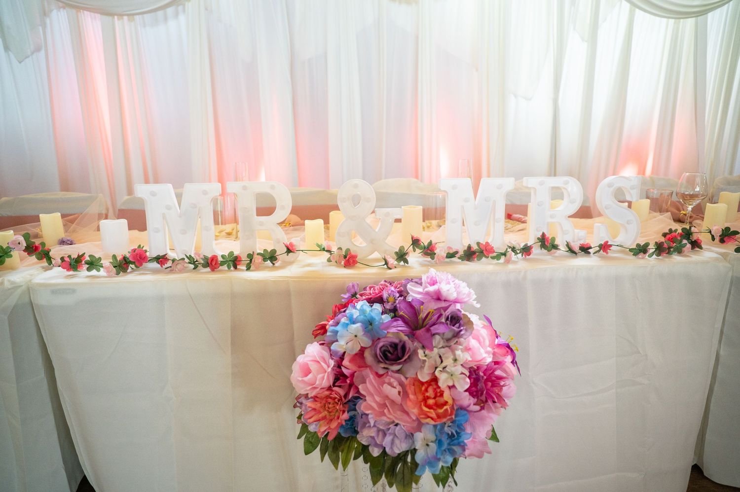Elegant wedding head table decorated with Mr & Mrs letters and colorful floral bouquet.