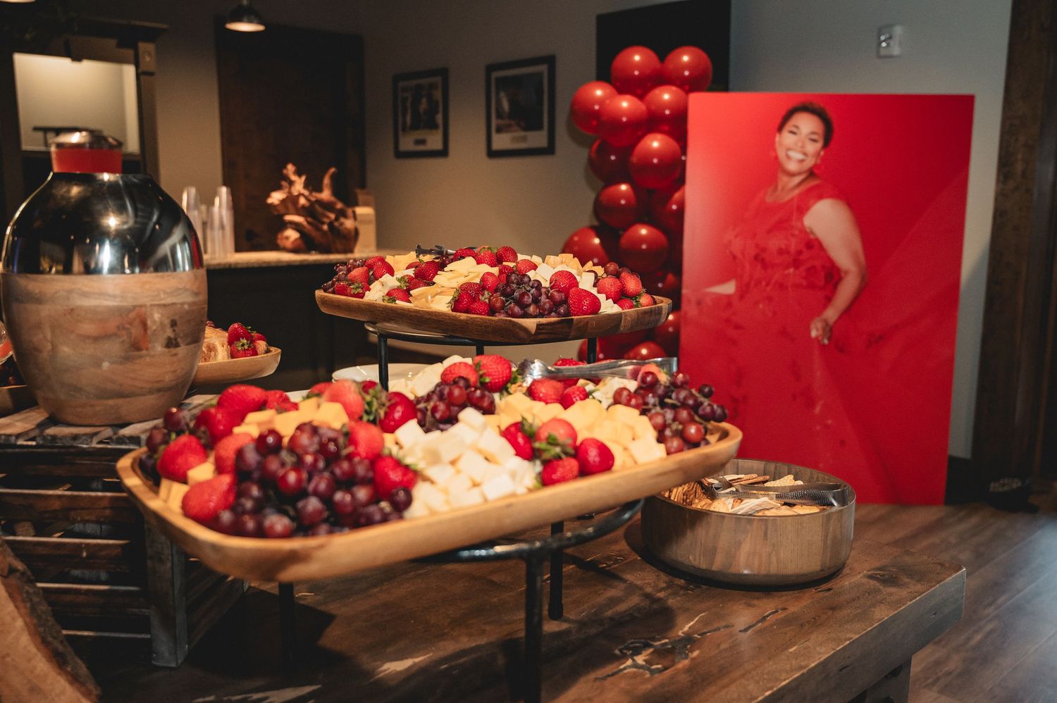 Fresh cherries and berries displayed in decorative wooden bowls on a rustic table with red backdrop.