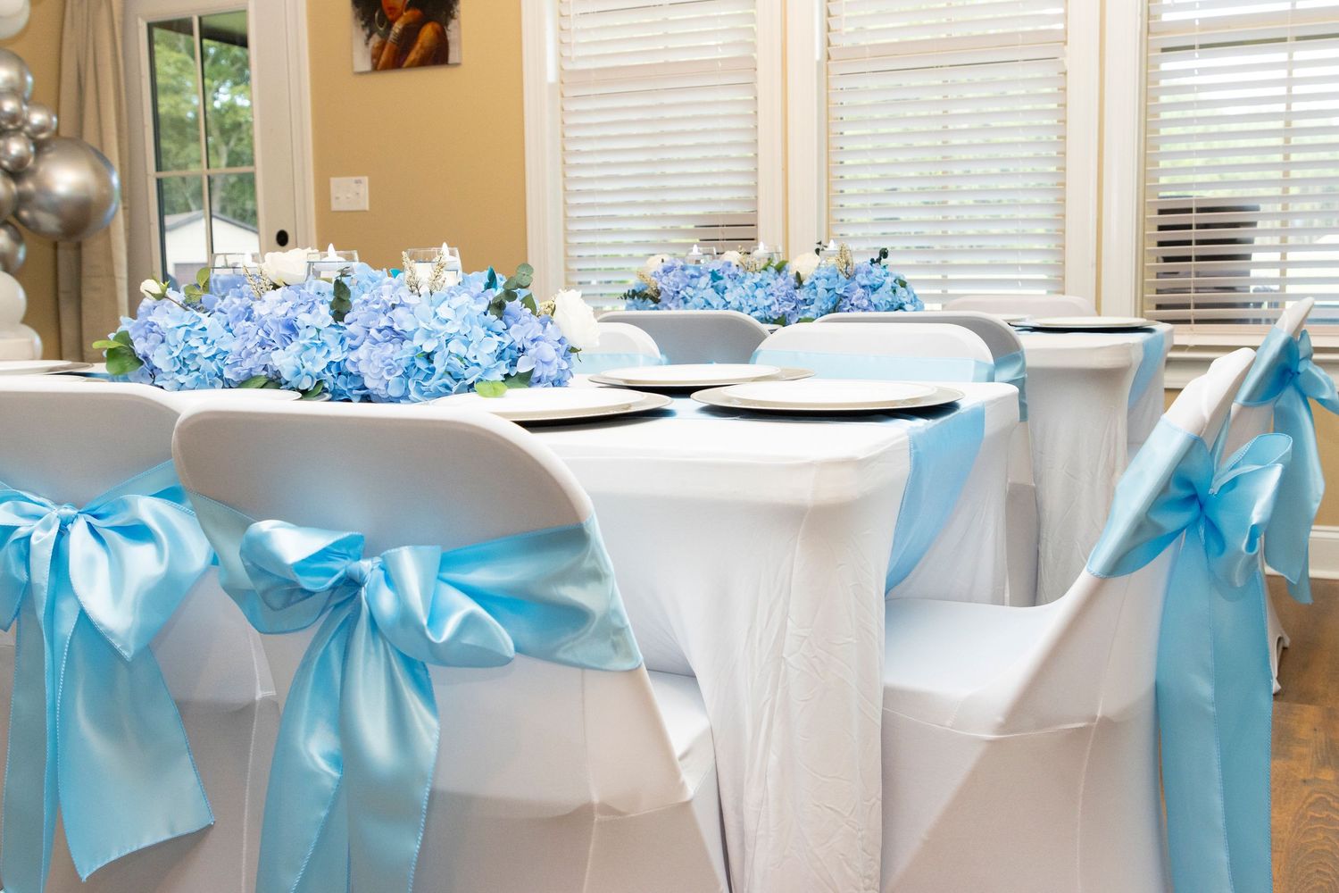 White spandex chair covers with turquoise blue satin bows and hydrangea centerpieces decorate an elegant reception table.
