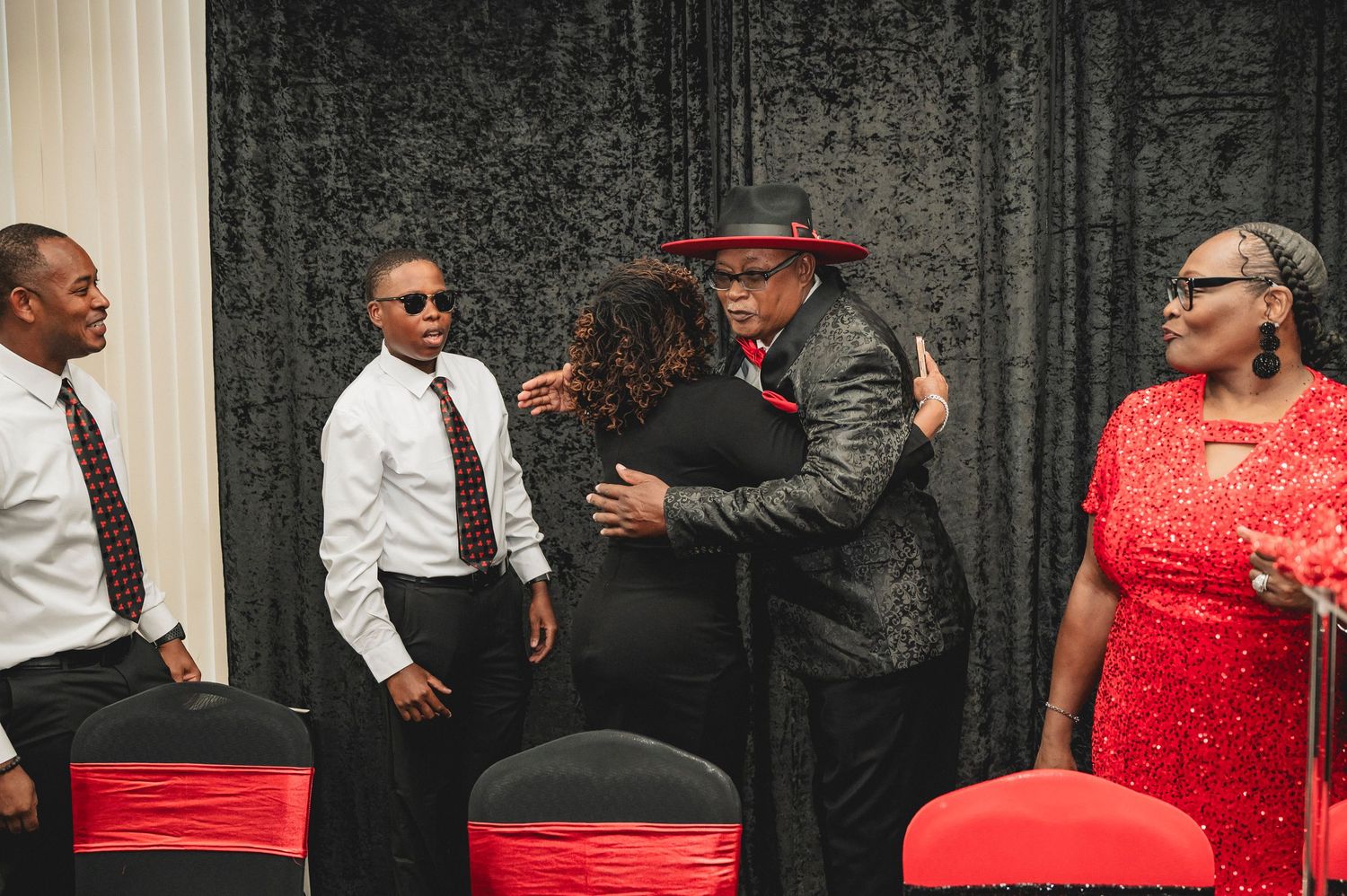 Party guests in formal attire mingling at an event with red and black decor.