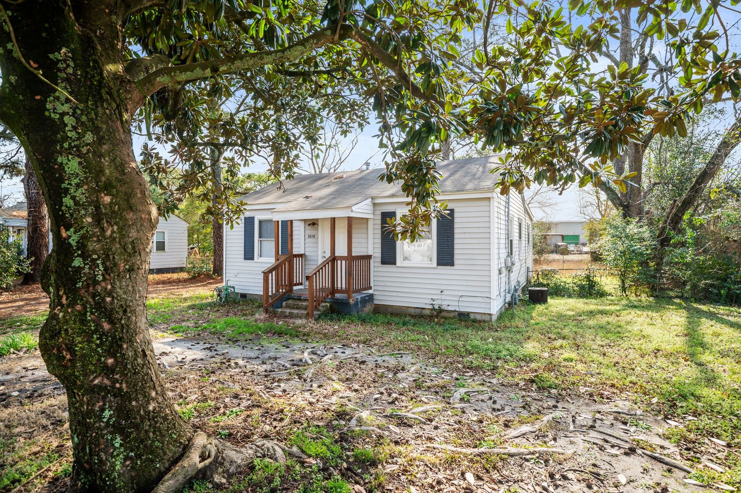 Small white cottage-style home with covered front porch, surrounded by mature trees and a spacious yard.