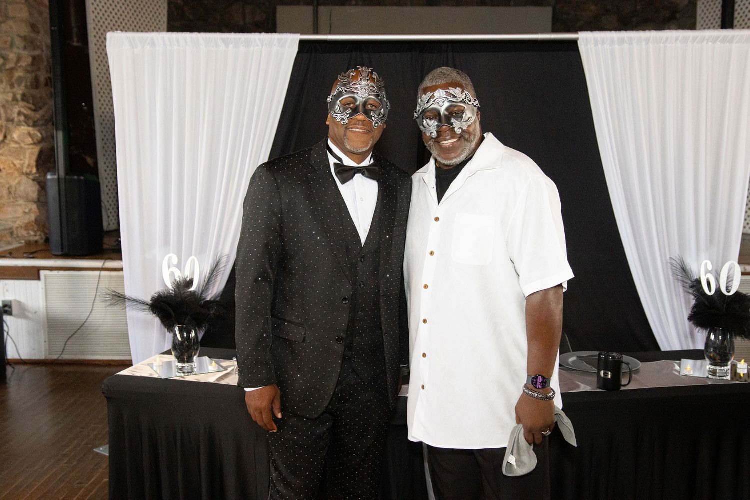 Two people in formal attire stand close together at an elegant event with white curtains in the background.