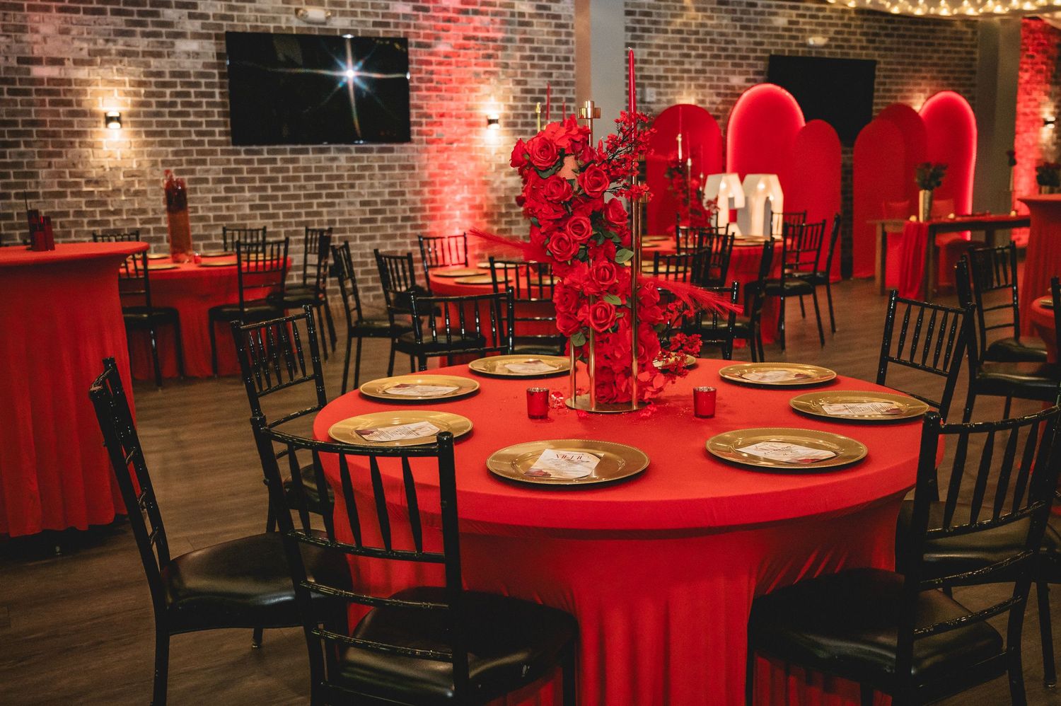 Romantic reception setup with red tablecloths, black chairs, and ambient lighting against exposed brick walls.