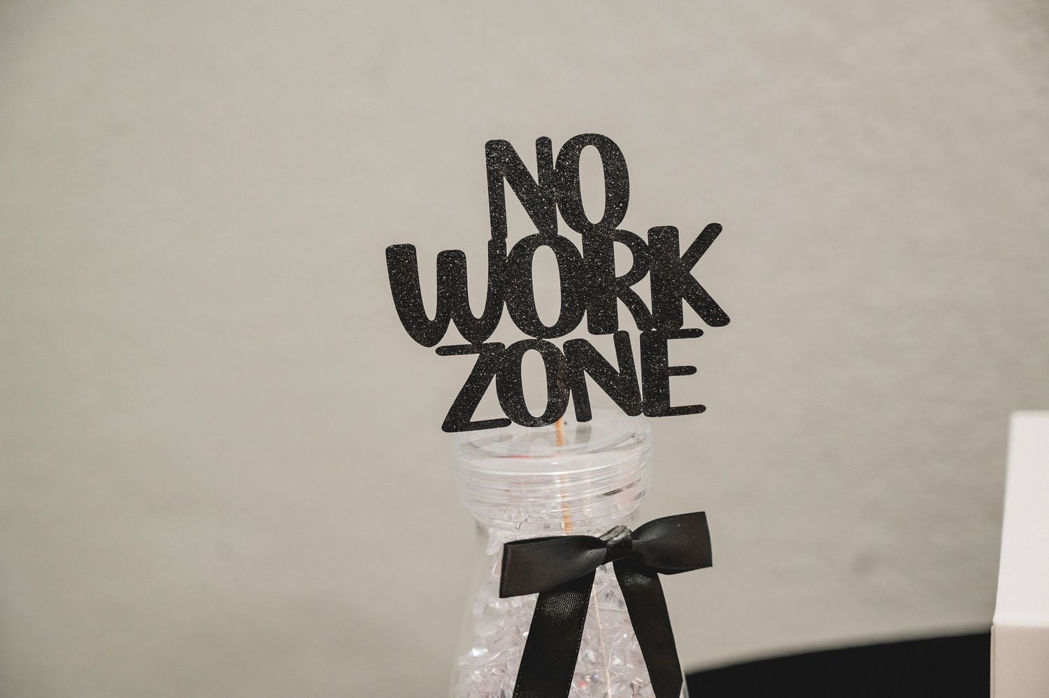 Black decorative sign reading 'NO WORK ZONE' with a bow tied underneath against a light colored wall.
