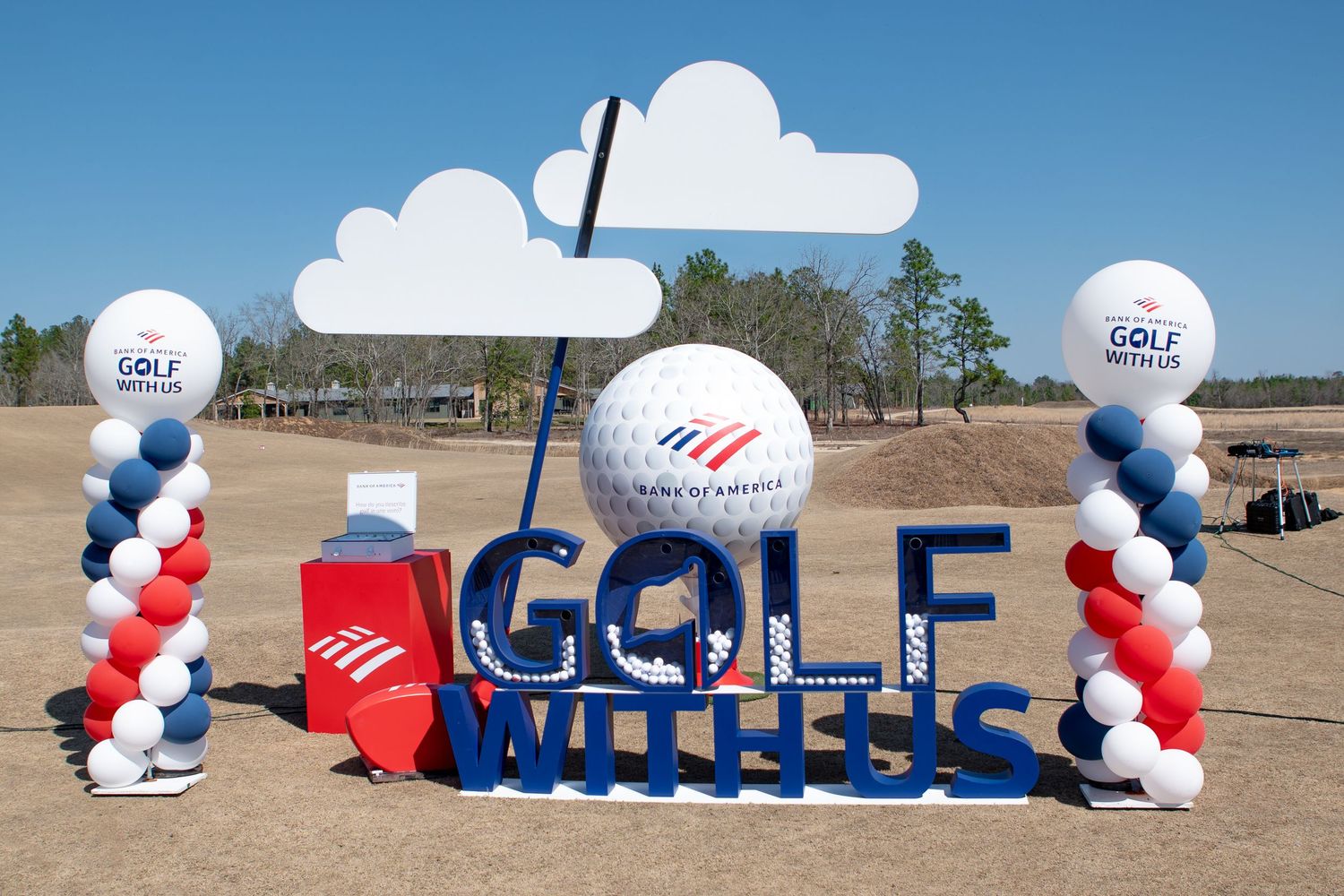 Red, white, and blue balloon arch decorations spell out GOLF at an outdoor event on a sunny day.