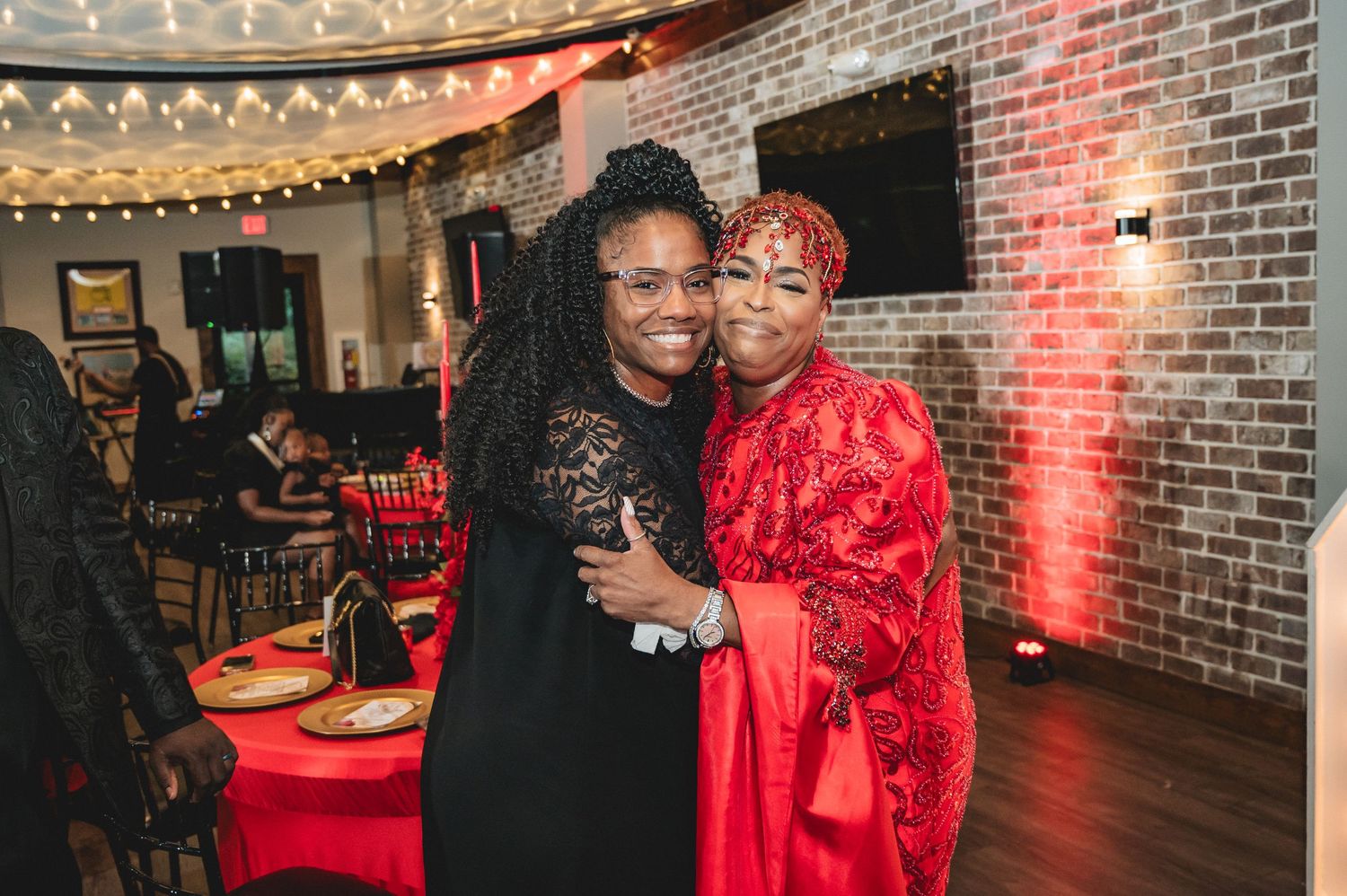 Party guests enjoy a festive celebration with red decorations and brick wall backdrop.