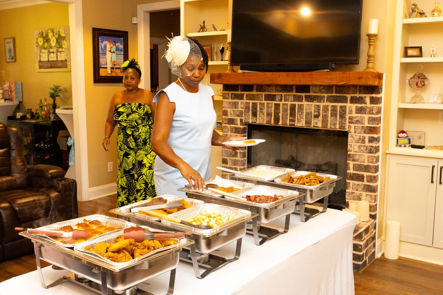 Catering setup with warming trays at an indoor event featuring a brick accent wall and TV.