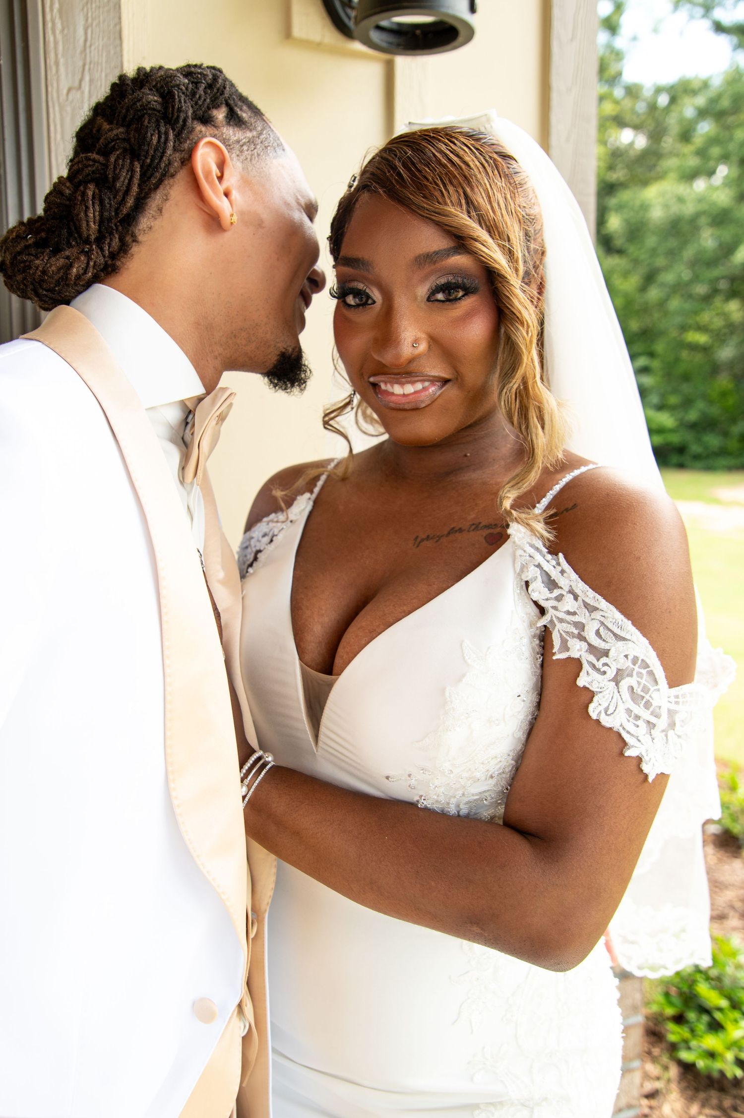 Bride in white lace wedding gown with veil smiling as groom leans in close.