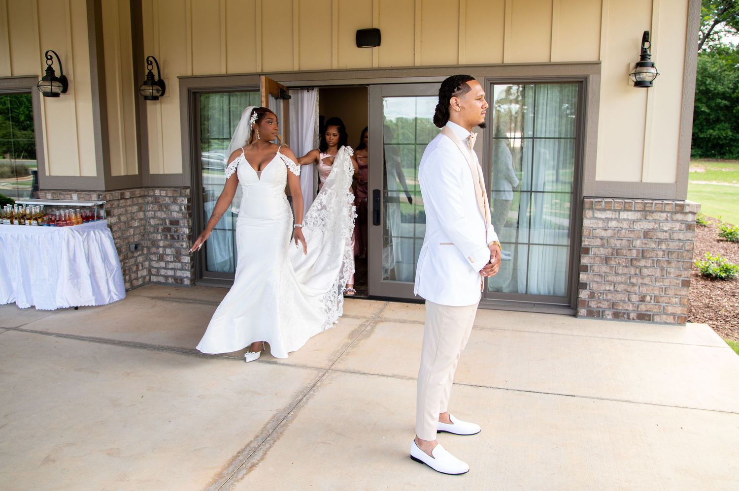 Bride in white gown and partner in white suit walking outside a brick wedding venue entrance.