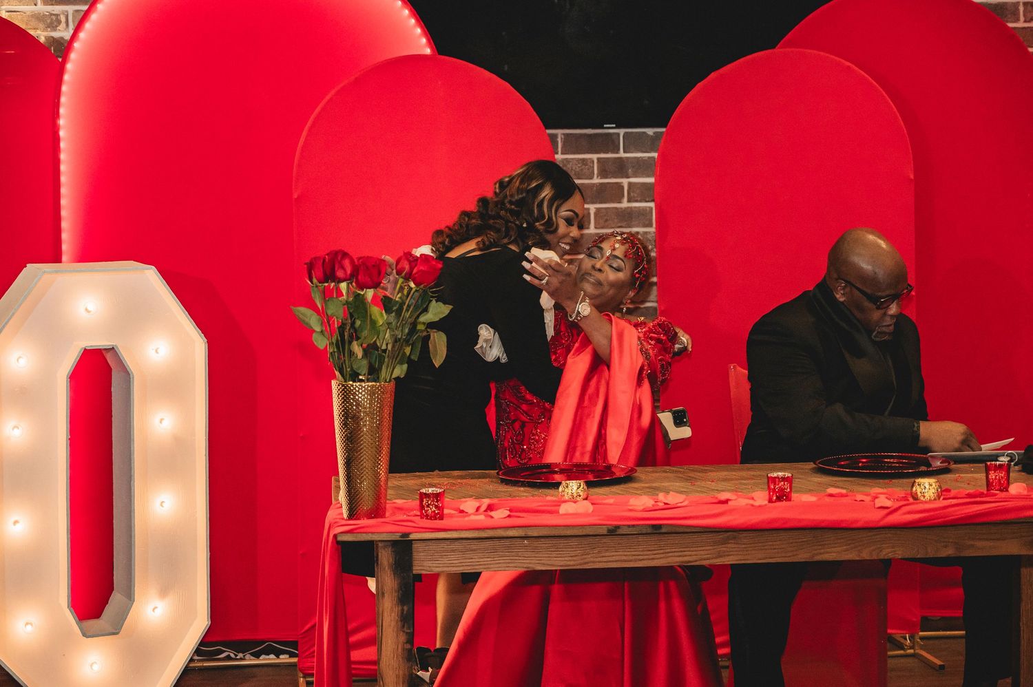 String lights illuminate a red-themed event space with elegant table settings and brick walls.