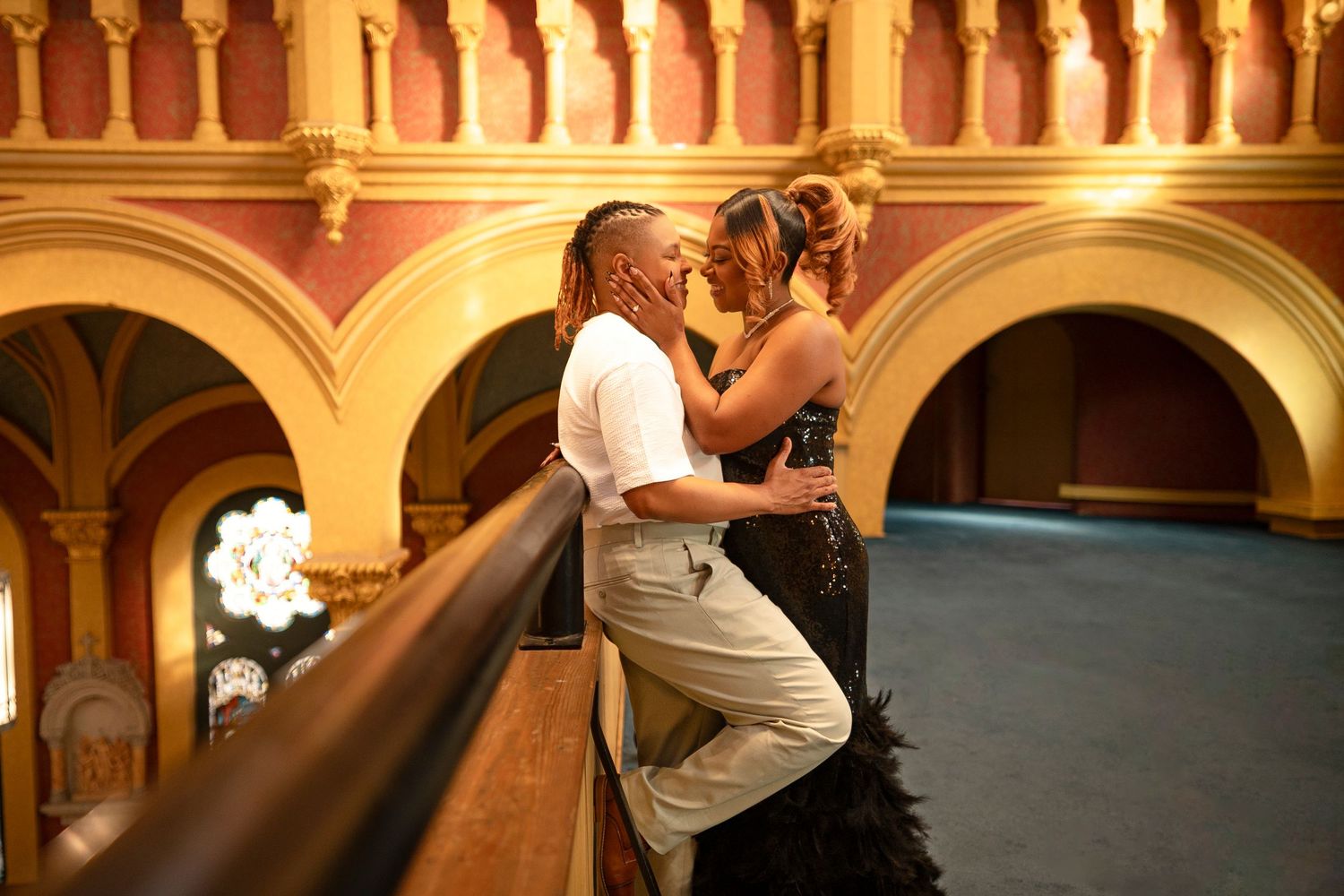 Romantic couple sharing an intimate moment on a balcony inside an elegant historic theater with ornate arches.