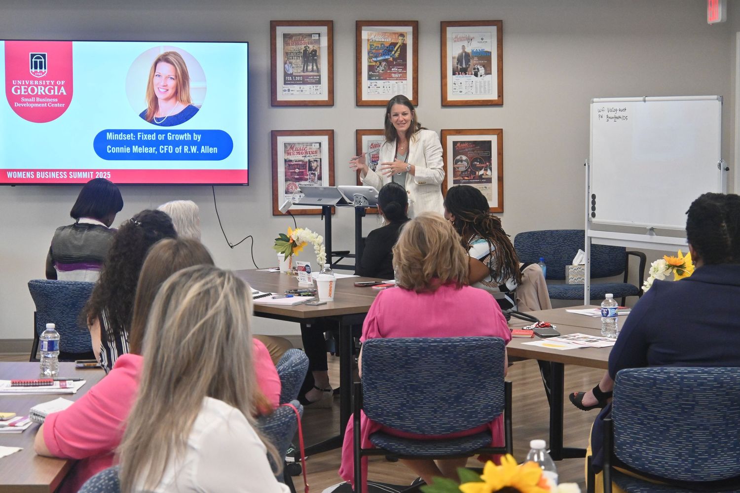 Woman presenting at a business seminar in Georgia, with attendees seated at tables and a presentation screen visible.