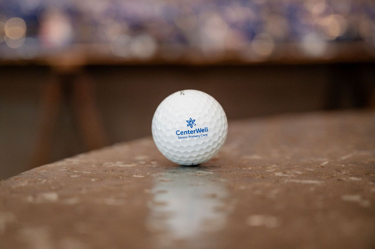 A white golf ball sits on a wooden surface with shallow depth of field creating a soft blurred background.