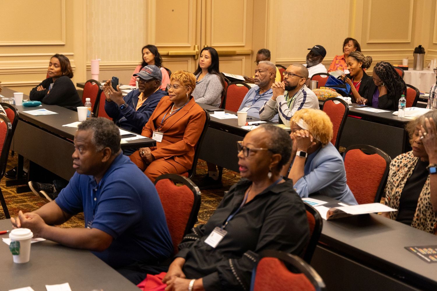 People sit in rows at a conference or training session in a lecture hall with red seats.
