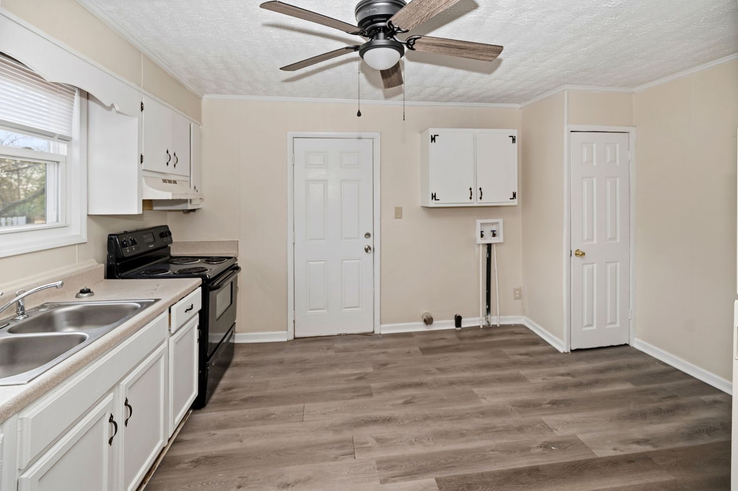 Kitchen with white cabinets, black electric range, sink, hardwood floors, ceiling fan, and multiple doors in a bright room.