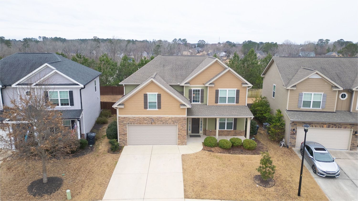Two-story brick and tan siding home with two-car garage, manicured landscaping, and suburban neighborhood backdrop.