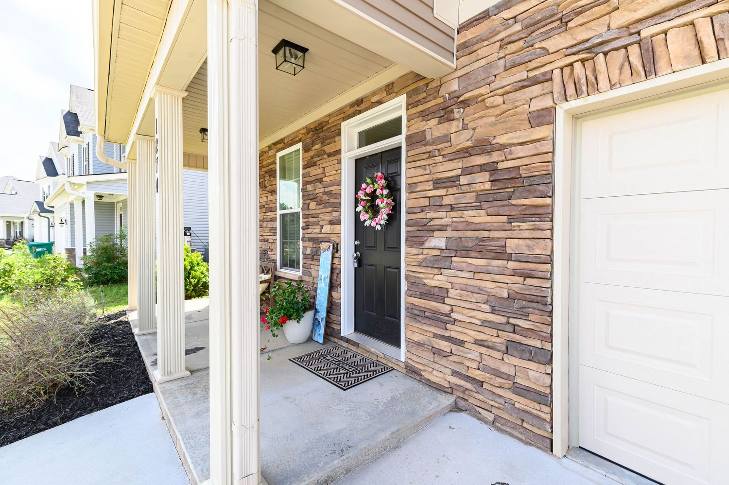Stone-accented home exterior with black front door, decorative wreath, and attached garage on a sunny day.