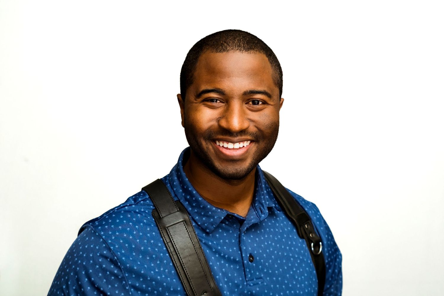 Professional wearing a bright blue patterned shirt smiles warmly against a white background.