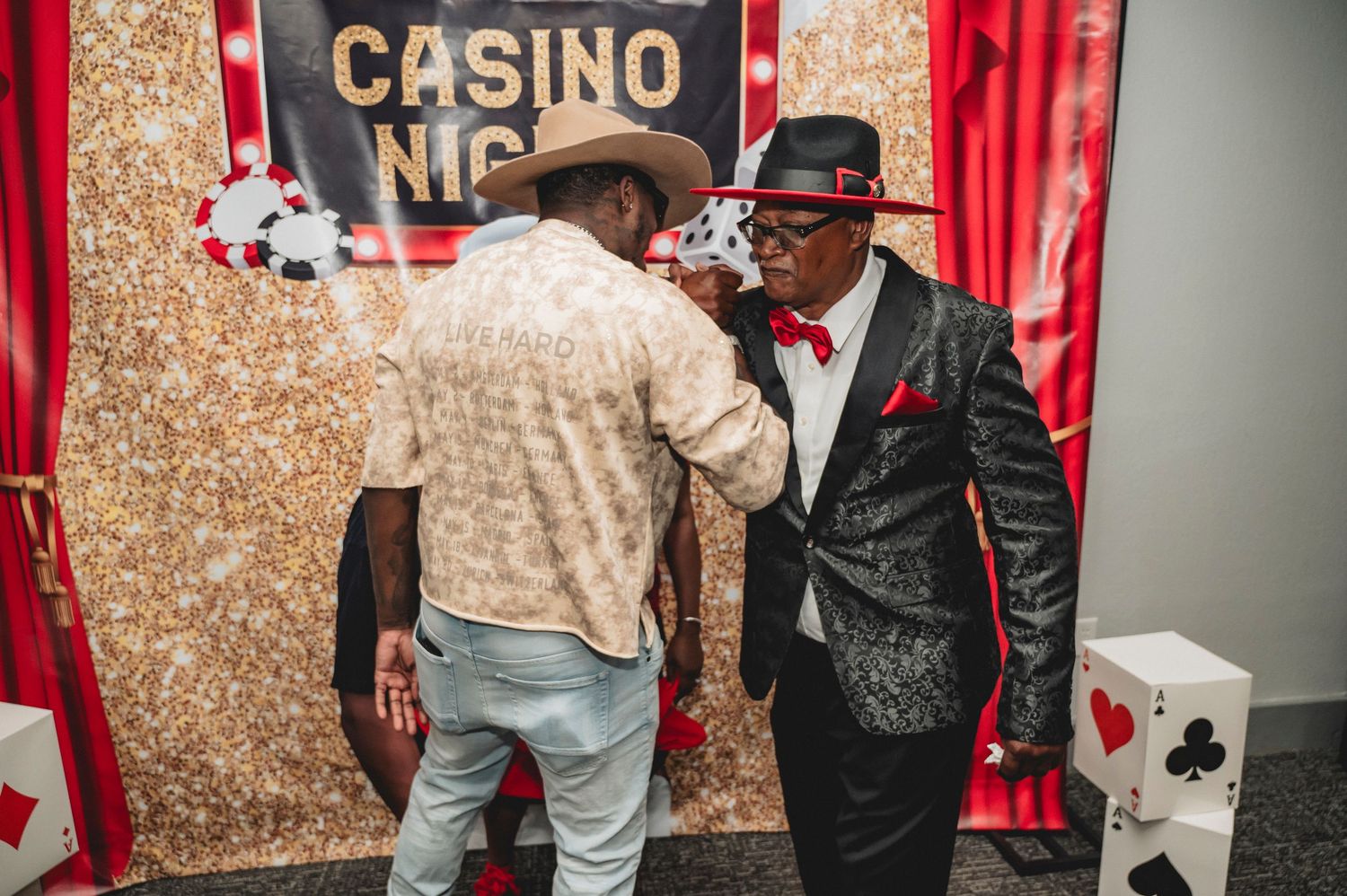 Casino night party decor featuring gold sequin backdrop and red curtains with elegant signage.