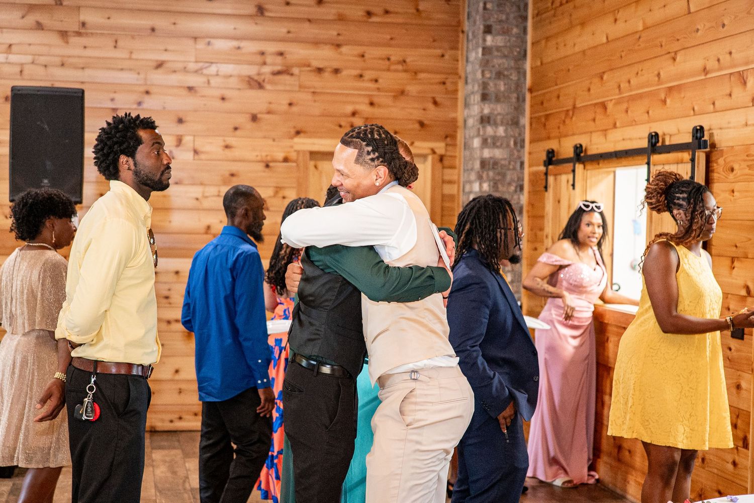 Wedding guests share warm embraces in rustic barn reception venue with barn doors.